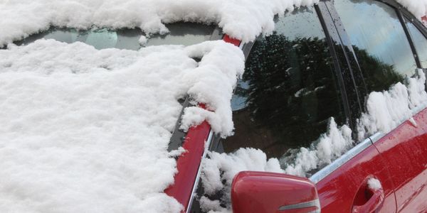 Verschneiter Außenspiegel und Seitenscheibe eines roten Autos