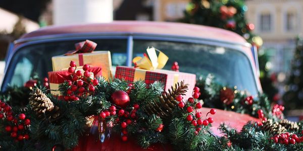 Motorhaube eines roten Autos mit Tannengirlande und eingepackten Geschenken